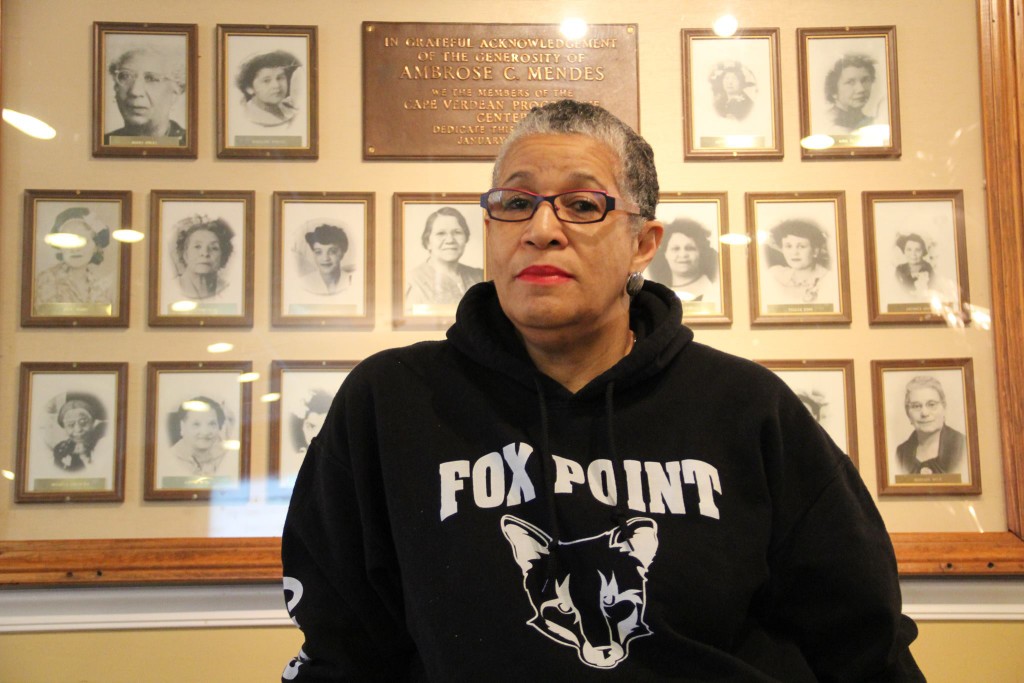 Claire Andrade-Watkins in a Fox point sweater in front of a wall of photos of other women. 